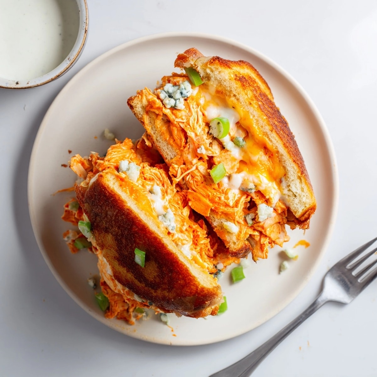 Golden, buttery Buffalo Chicken Grilled Cheese sandwich, sliced open; dipping sauces nearby.