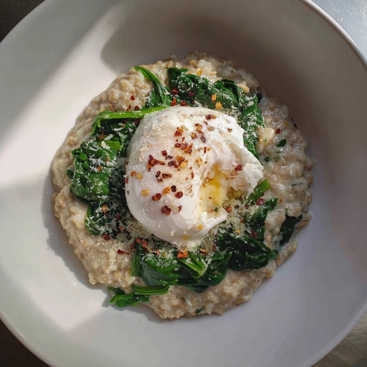 A close-up of savory oatmeal, showcasing wilted spinach and a glistening poached egg yolk.