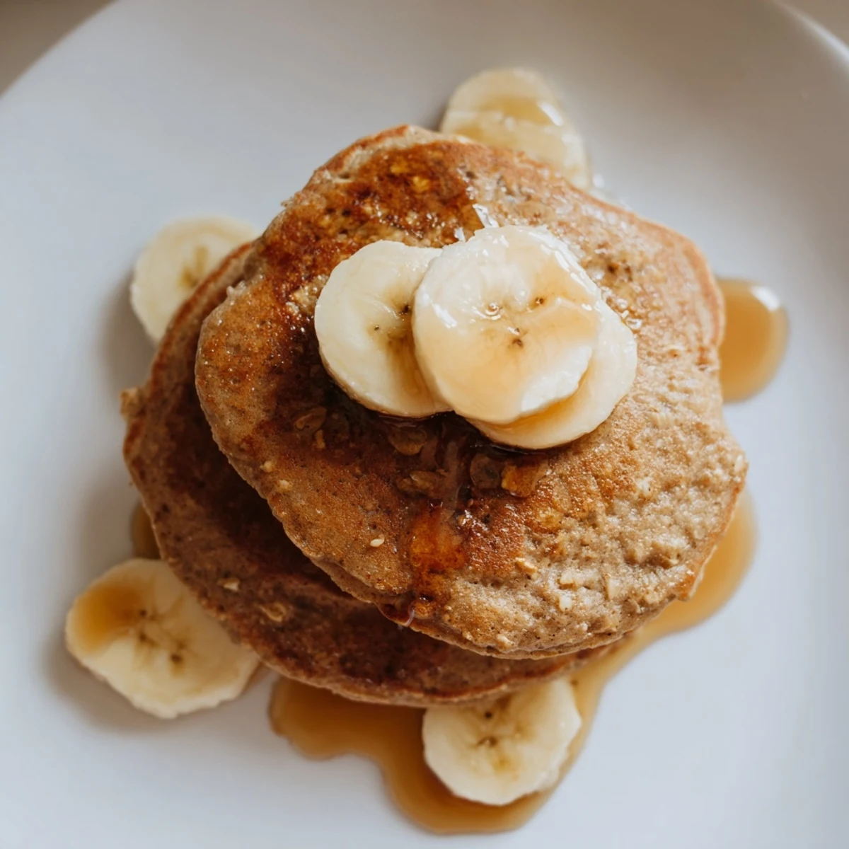 Golden-brown banana oat pancakes stacked high, ready to be drizzled with sweet maple syrup.