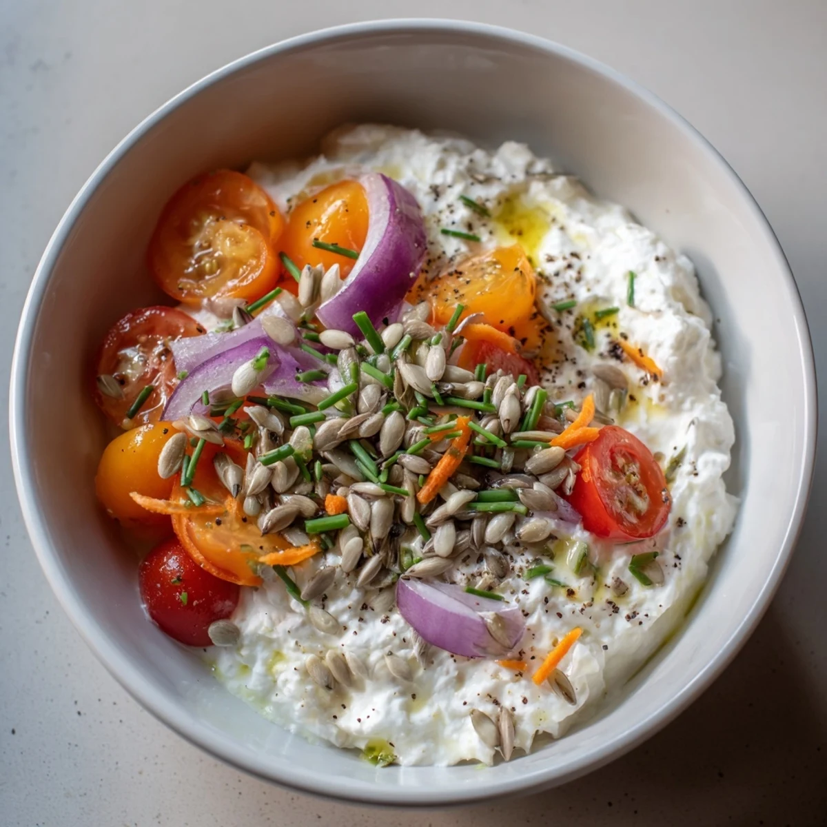 Creamy cottage cheese snack bowl with fresh veggies, olive oil, and crunchy sunflower seeds.