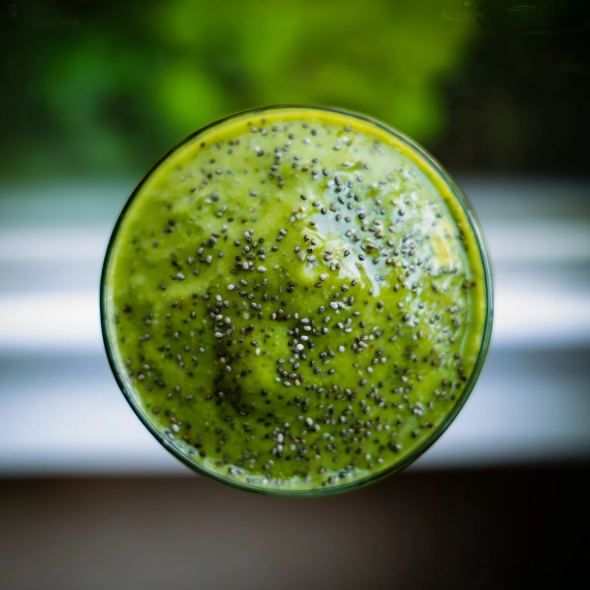 The green detox smoothie pours smoothly from a blender into two glasses, creamy from banana, bright with mint, and garnished with a leaf.