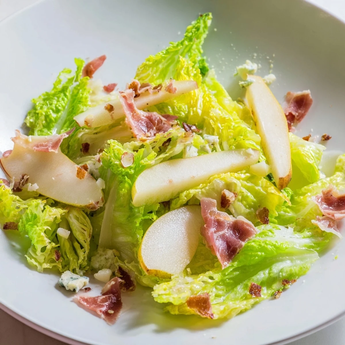 A vibrant Frisée, Pear, Blue Cheese, and Crispy Prosciutto Salad arranged with crisp lettuce, ripe pear slices, and crunchy prosciutto shards.