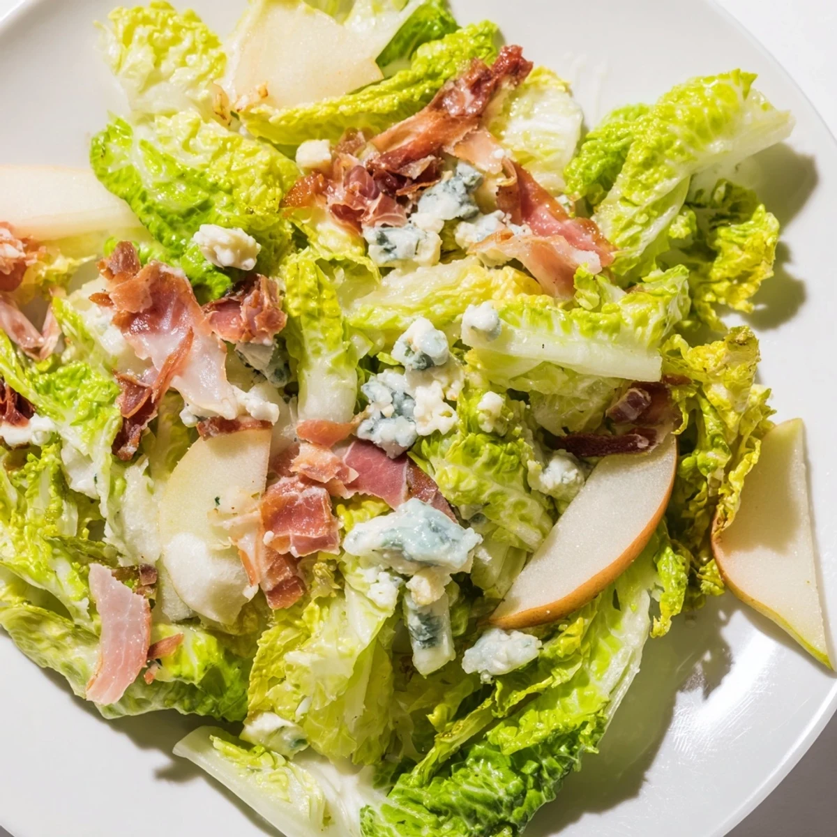Elegant plated Frisée, Pear, Blue Cheese, and Crispy Prosciutto Salad drizzled with tangy vinaigrette, served with white wine as a light lunch.