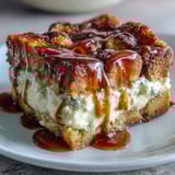 A close-up of golden Caramel Cream Cheese French Toast Casserole on a plate, topped with whipped cream and fresh raspberries for brunch.
