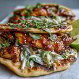 Golden glazed chicken, fresh cilantro, and lime wedges garnish these fusion naan chicken tacos.