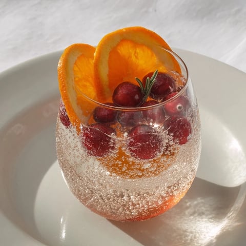 Festive snow globe mocktail with frozen cranberries garnished with rosemary sprigs, ready to serve.