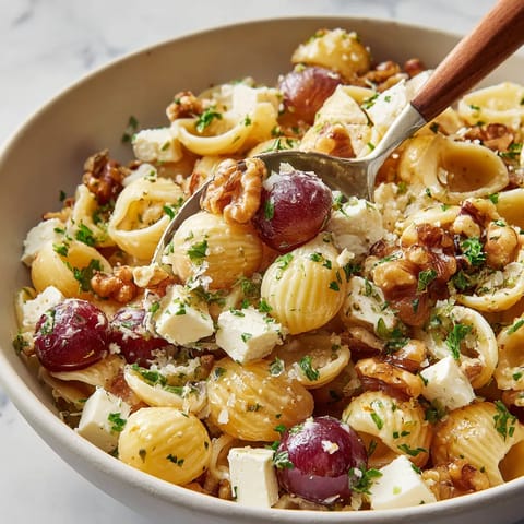 A bowl of pasta with grapes and walnuts.
