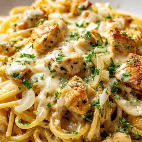 A plate of spaghetti with chicken and onions.