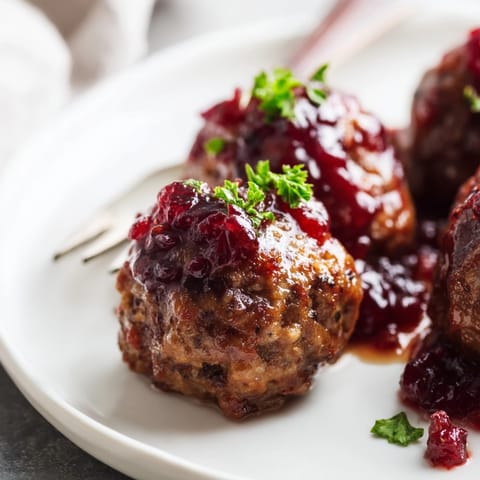 Shiny, saucy Sweet & Savory Cranberry Meatballs, baking sheet background, invite a festive bite.