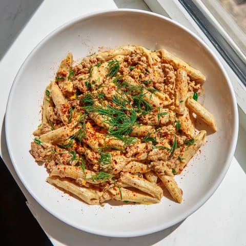 A close-up of a vibrant Turkish Pasta with Ground Turkey, garnished with fresh herbs and butter.