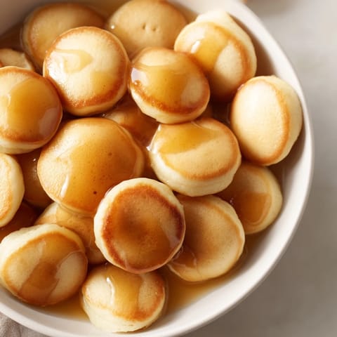 Mini, golden brown pancake cereal, a bowl filled with delightful bite-sized pancakes and syrup.