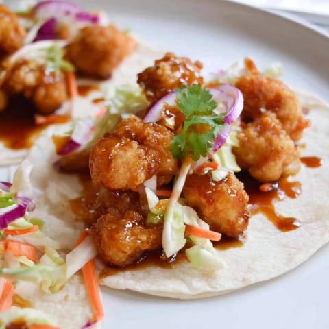 A close-up shot of delicious Hot Honey Chicken Tacos, overflowing with slaw and fresh cilantro.