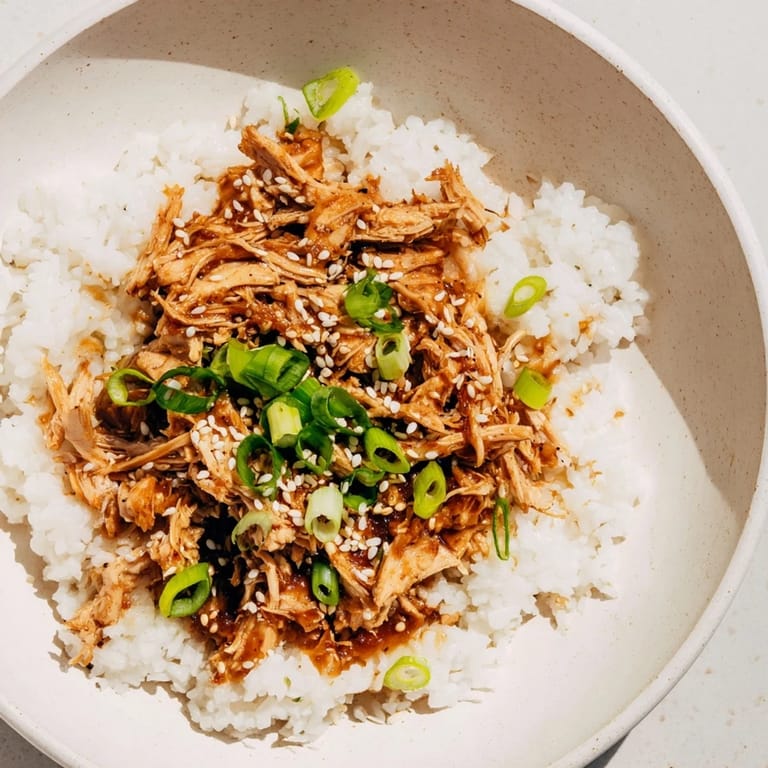 A steaming bowl of comforting teriyaki chicken over rice, garnished with green onions; a delightful aroma.