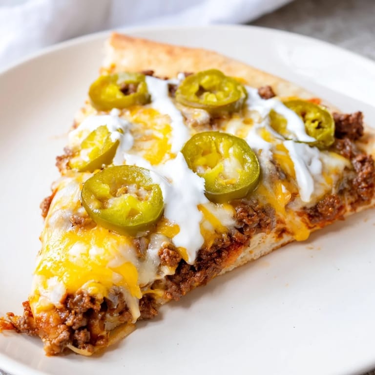 Golden-crusted ground beef taco pizza, perfect for a family dinner with a creamy drizzle on top.